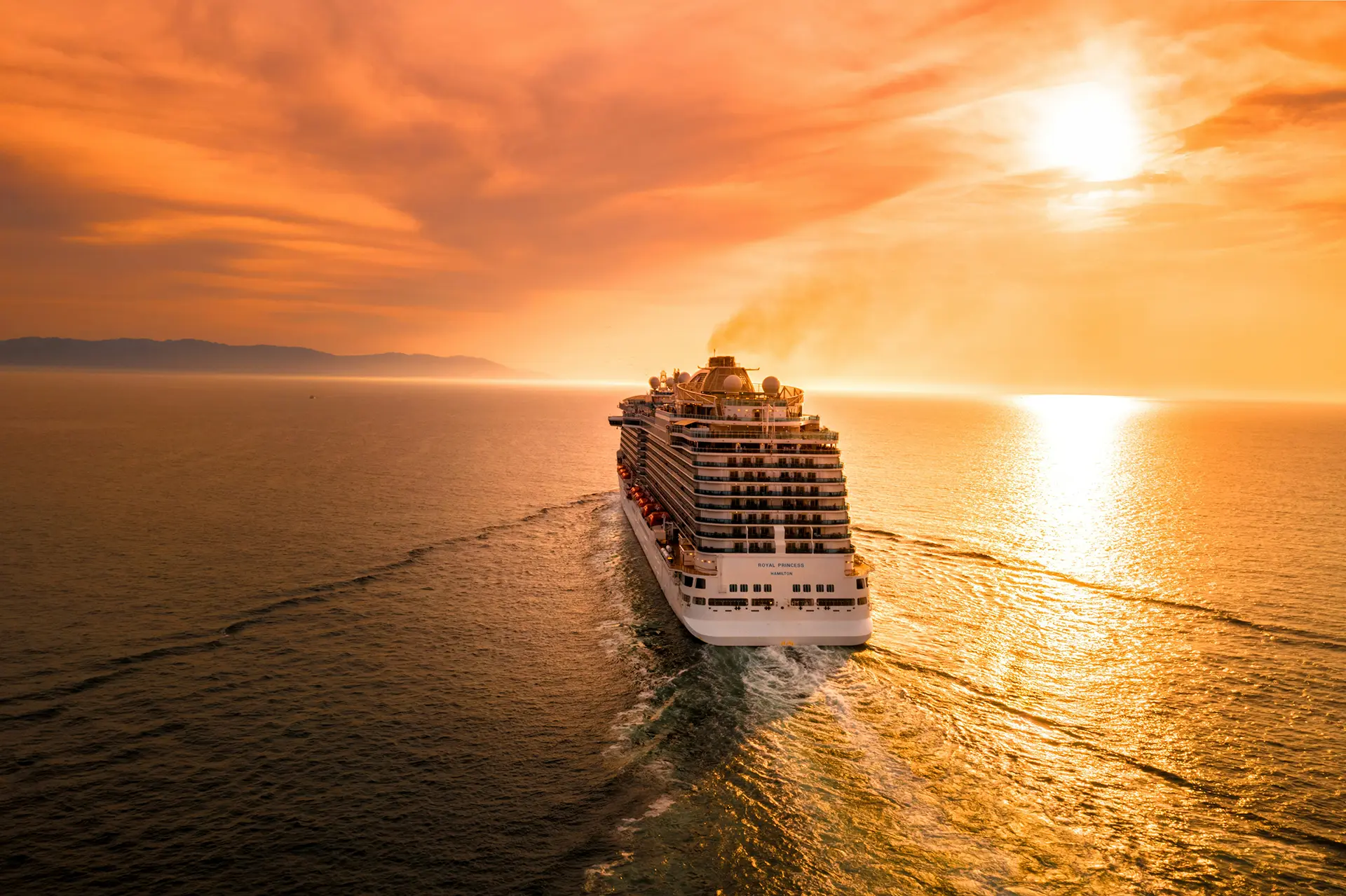 Cruise ship on a calm ocean with a bright orange and yellow sunset