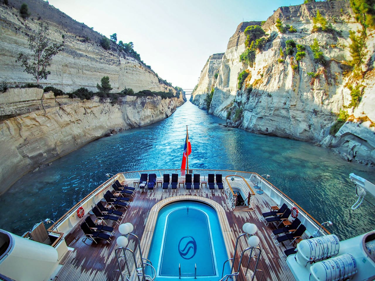 View of the top deck on to a pool at the back of a cruise in a narrow bay with cliff sides on either side.